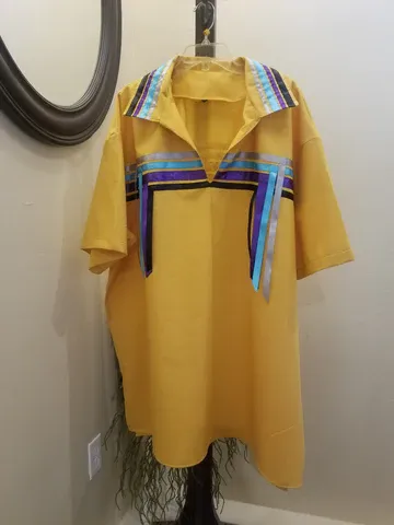 A yellow shirt is hanging on a hanger next to a mirror.