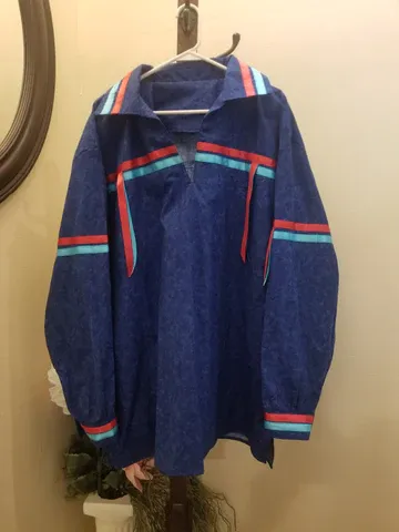 A blue jacket with red , blue and white stripes is hanging on a hanger.