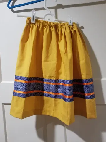 A yellow skirt with blue and orange stripes is hanging on a hanger