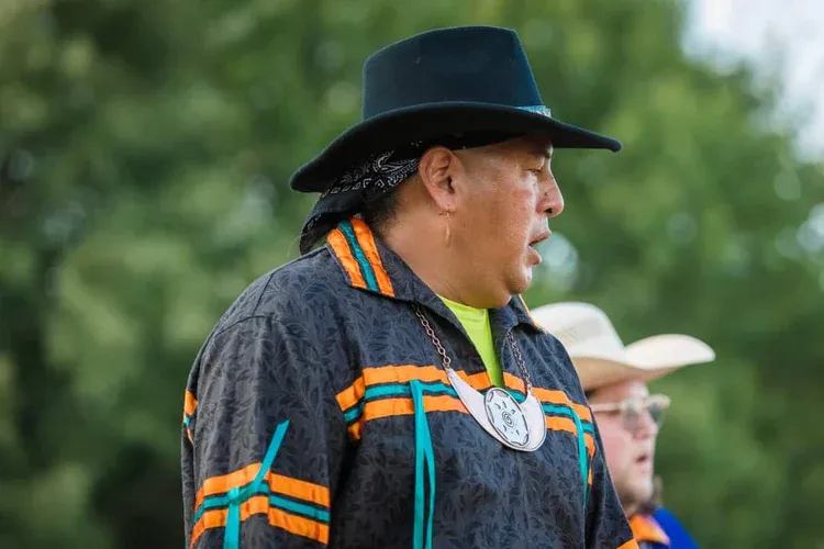 A man wearing a hat and a jacket is standing next to another man wearing a cowboy hat.