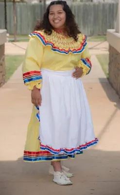 A woman in a yellow dress and white skirt is standing on a sidewalk.
