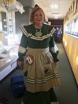 A woman in a green dress and apron is standing in a hallway.
