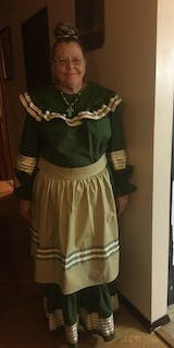 A woman in a green dress and apron is standing in a hallway.