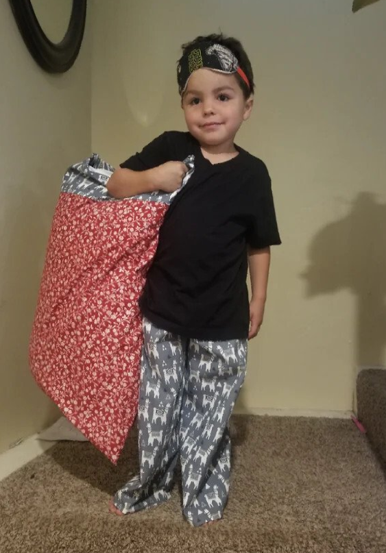 A young boy wearing pajamas and a headband is holding a pillow