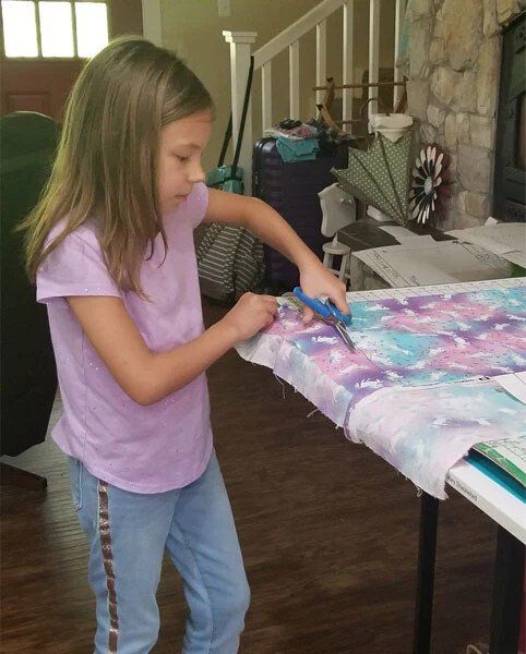 A little girl is cutting a piece of fabric with scissors