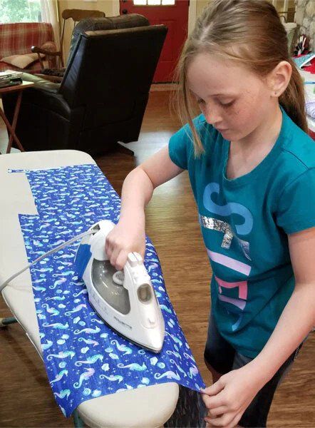 A girl wearing a shirt that says sixty is ironing a piece of fabric