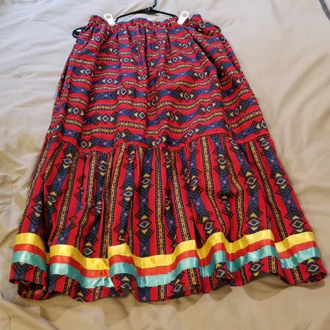 A red and blue skirt is hanging on a hanger on a bed.