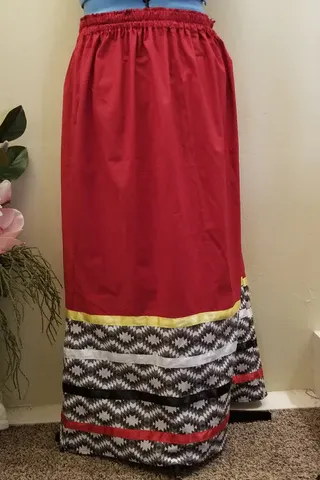 A red skirt with a black , white , and gold border is on a mannequin.