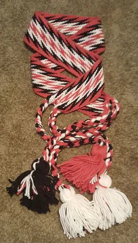 A red , white and black sash with tassels is sitting on a carpet.