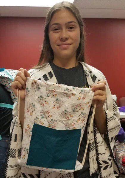 A girl is holding a piece of fabric in her hands which she made a bag.
