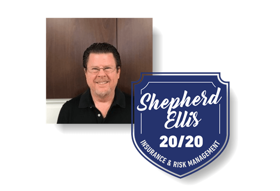 A man is standing next to a blue sign that says shepherd ellis 20/20