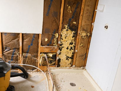 Damaged bathroom wall with exposed wood and insulation beside a tub and toilet area