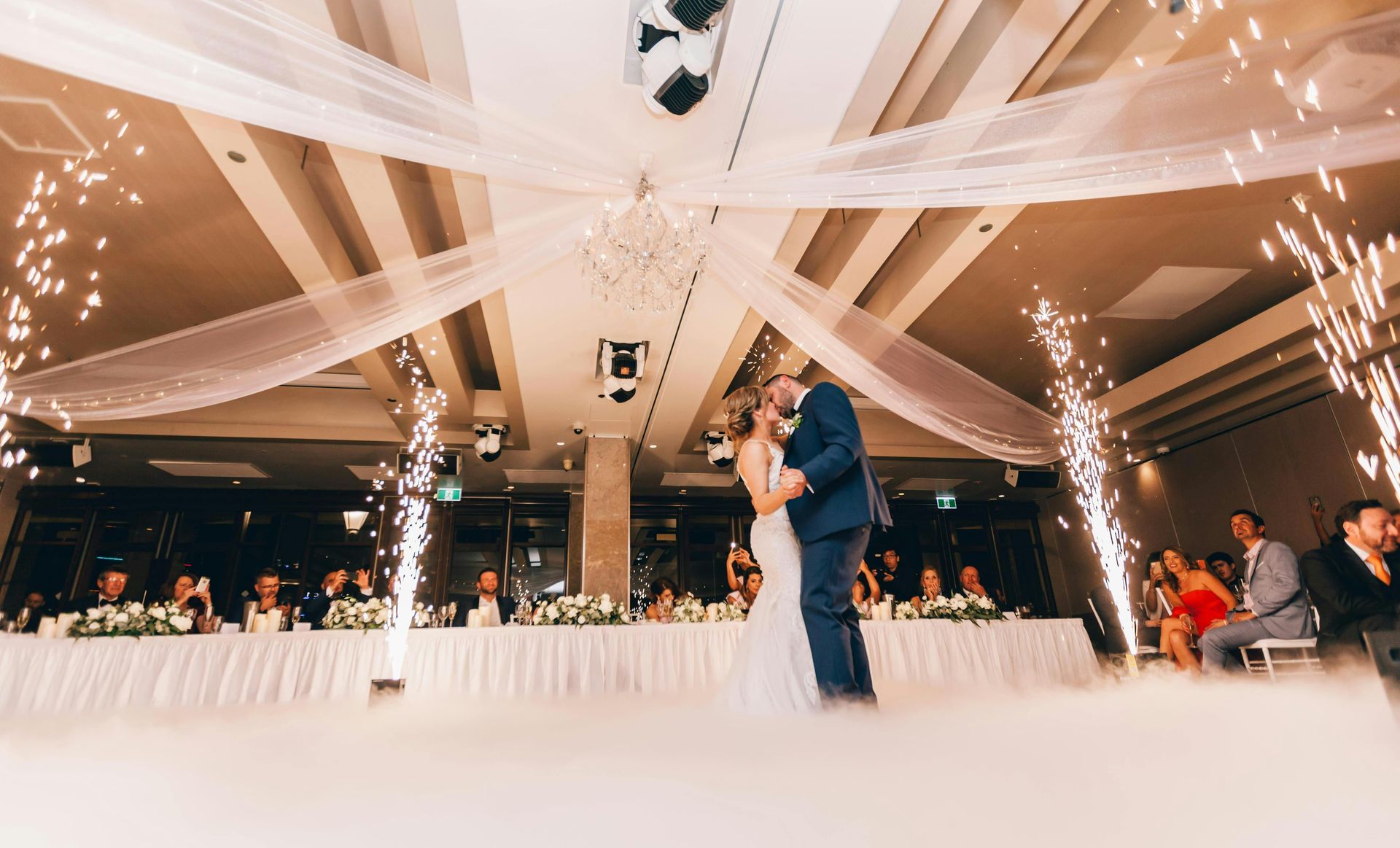 A bride and groom are dancing in front of a long table at their wedding reception.