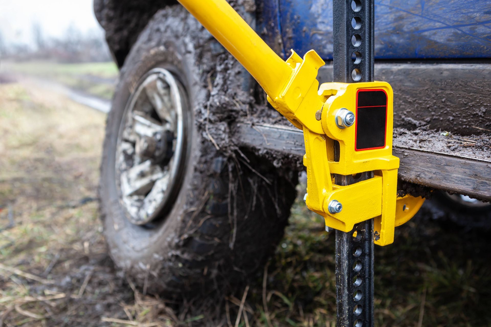 A yellow high lift jack is attached to the side of a muddy truck.