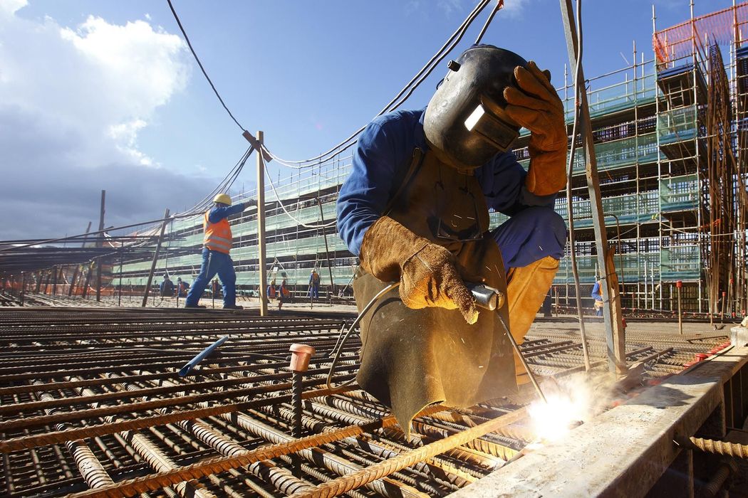 A man wearing a welding helmet is welding a piece of metal on a construction site.