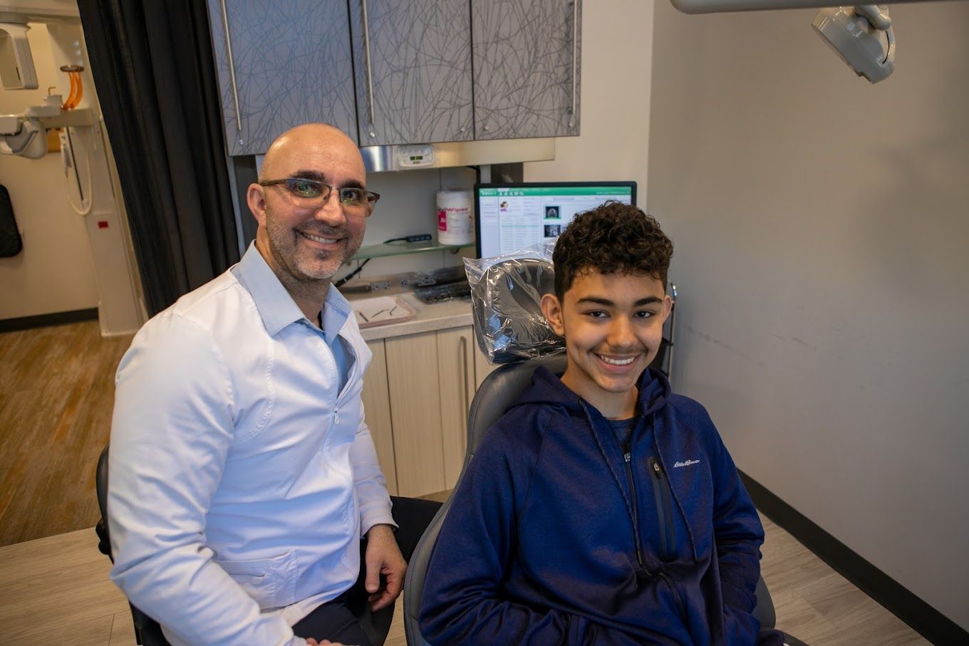 A dentist is sitting next to a young boy in a dental chair.