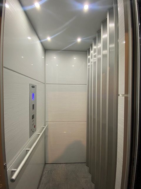 A white elevator is in the middle of a hallway next to a staircase.
