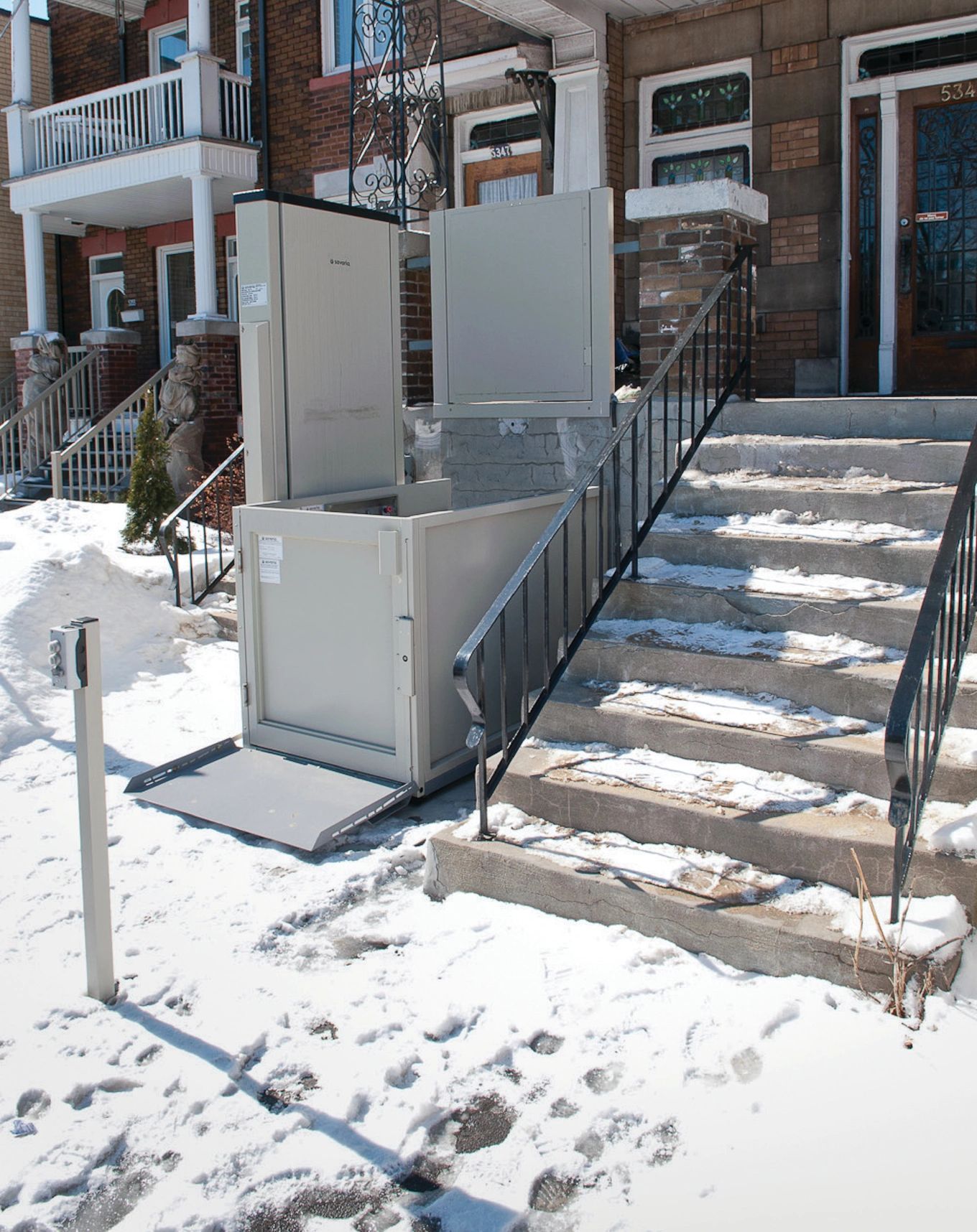 A stair lift is sitting outside of a house in the snow.