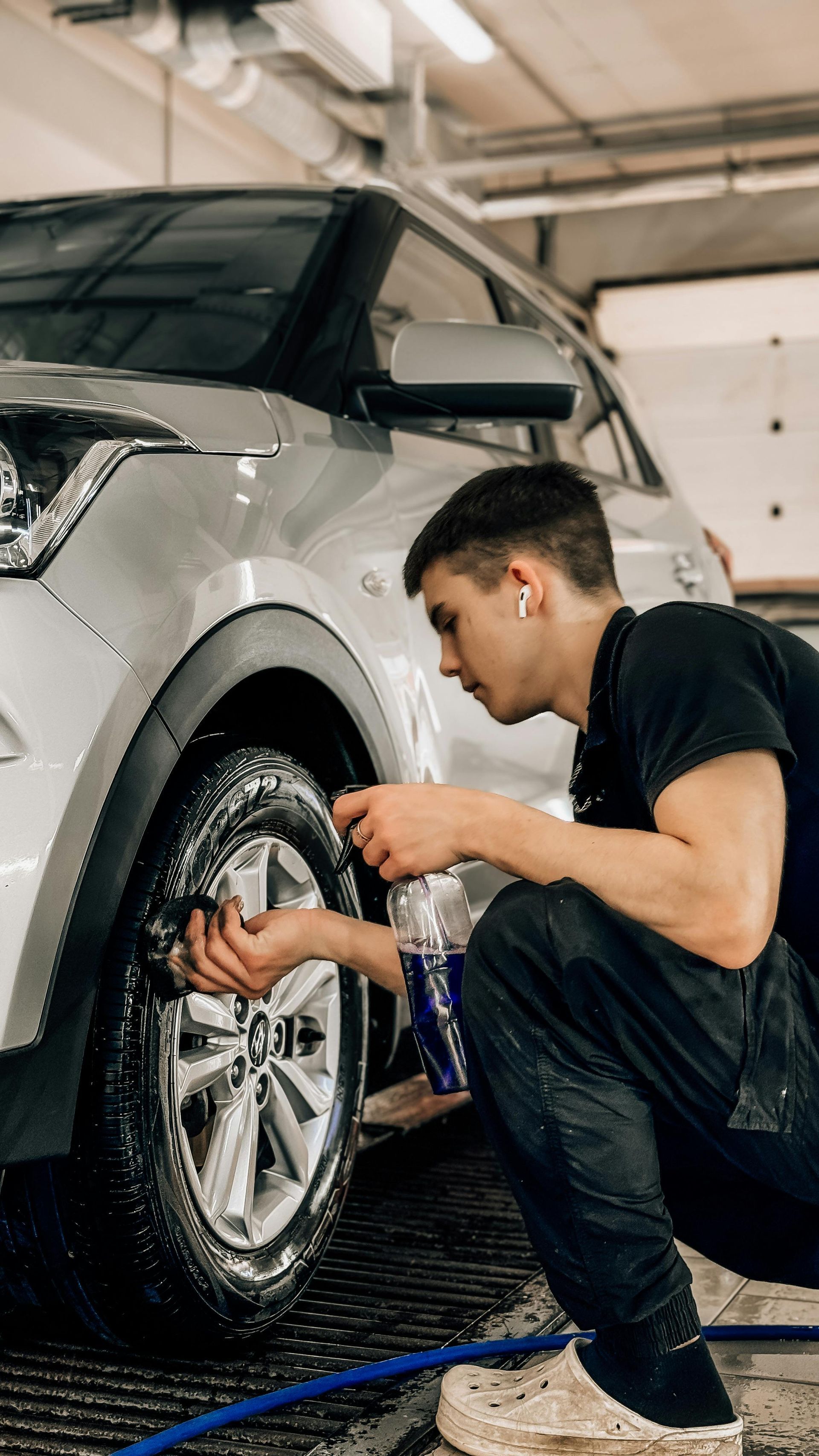 A man is cleaning the tires of a car in a garage.
