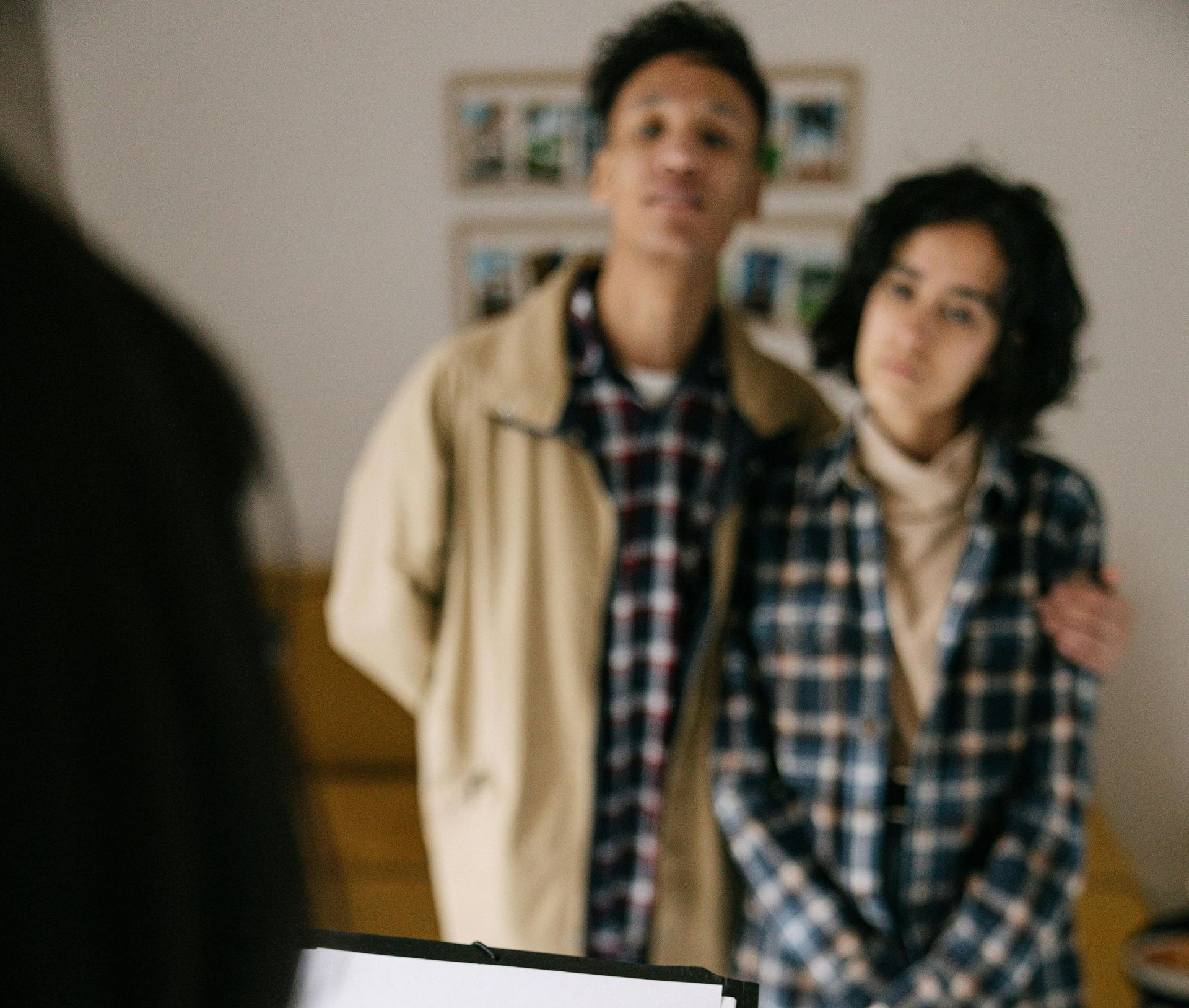 Young couple standing near a table, looking up, indoors; man's arm around woman's shoulders.