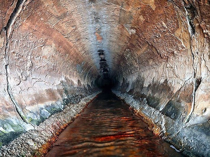Uno stretto tunnel roccioso con un canale d'acqua scura che lo attraversa
