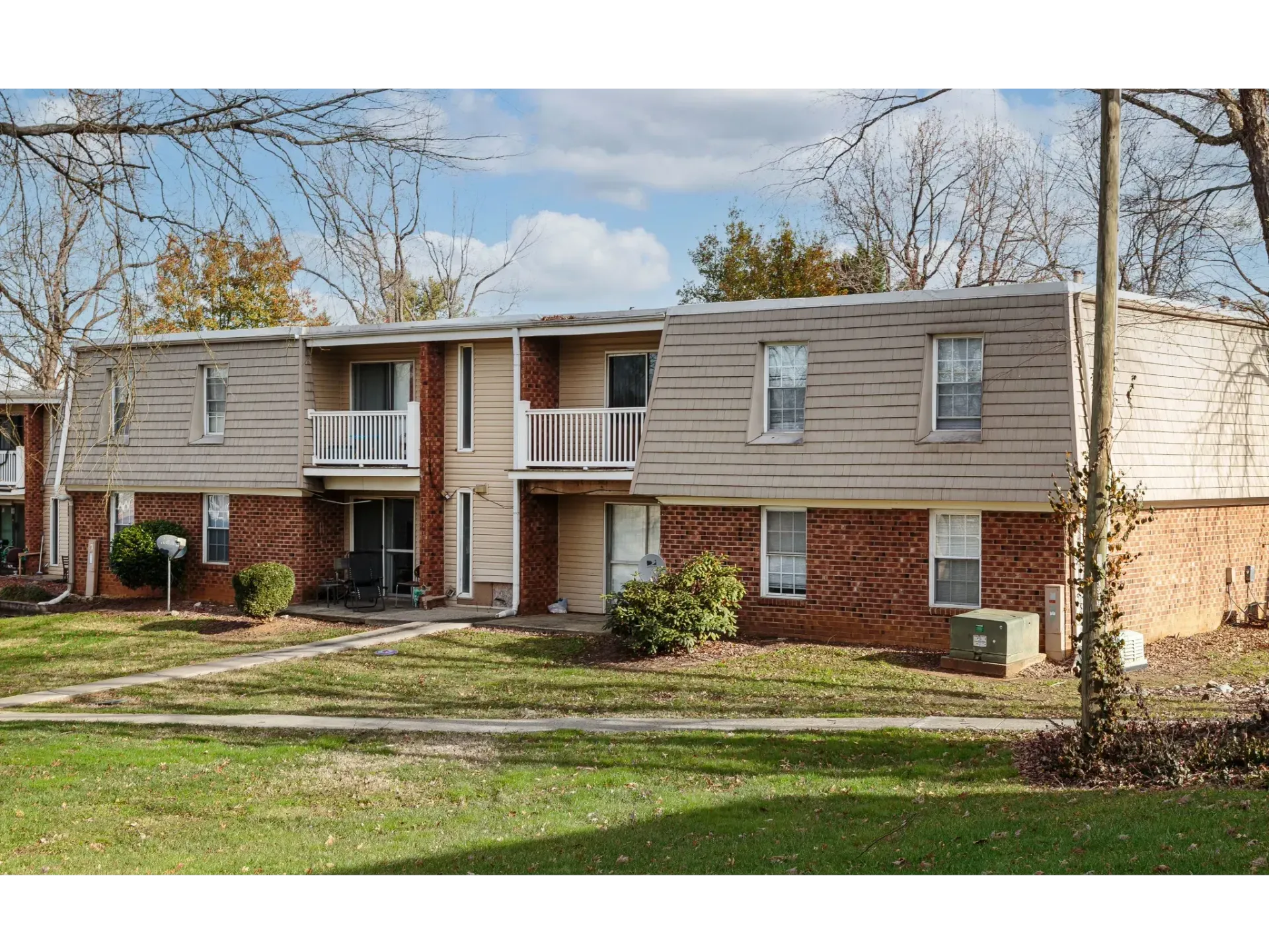Two-story brick apartment building with balconies and bare trees in front