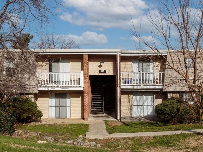 Two-story apartment building with brick exterior, balconies, and central staircase under a partly cloudy sky