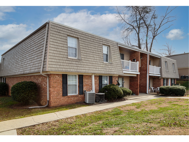 Two-story brick and gray apartment building with balconies and sidewalk under a partly cloudy sky