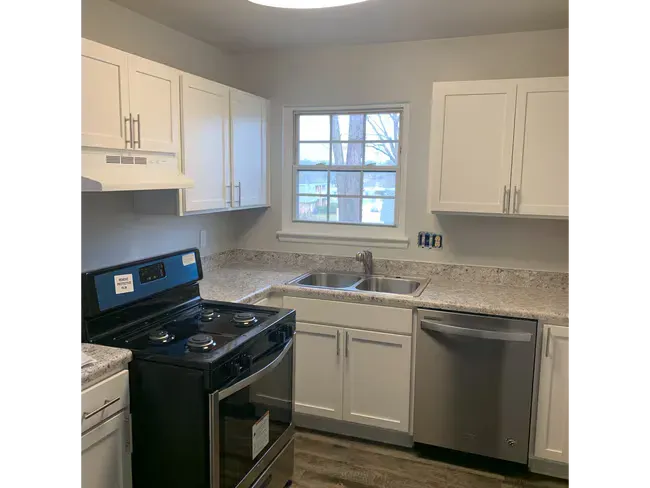 Modern white kitchen with black stove, stainless dishwasher, and window over the sink