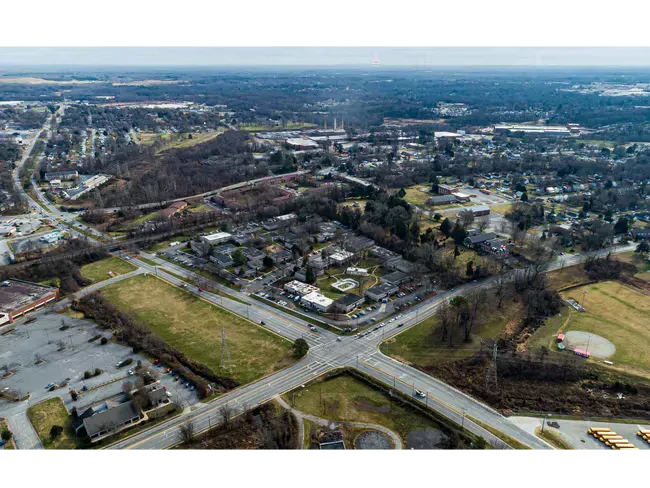 Aerial view of a suburban neighborhood with roads, houses, fields, and trees under a hazy sky