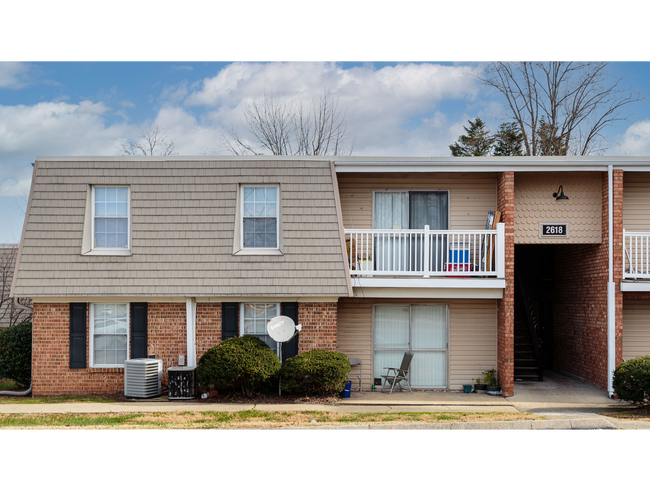 Two-story brick apartment building with tan siding, balcony, garage, and bare trees outside