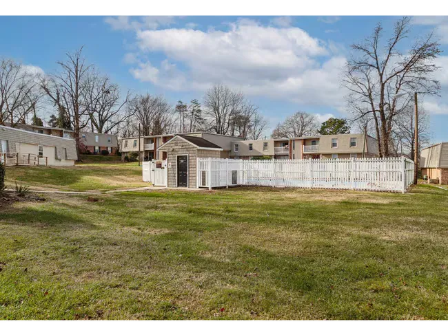 Wide grassy yard with a white fence and small buildings under a blue sky