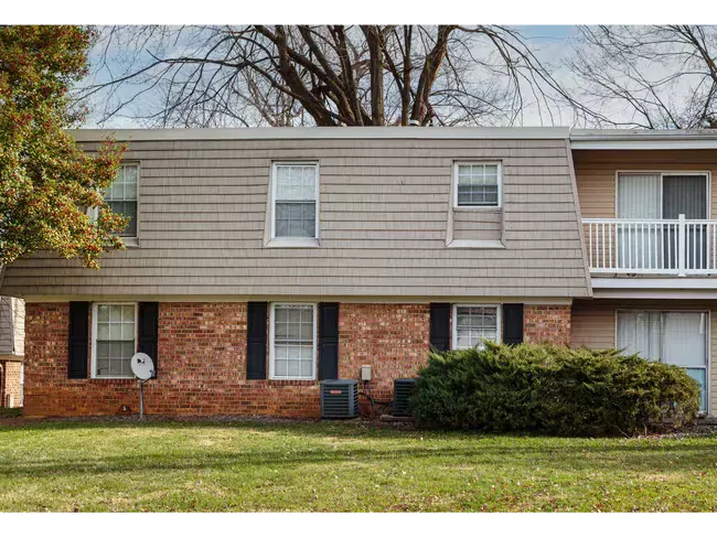 Two-story apartment building with brick and tan siding, balcony, and front lawn