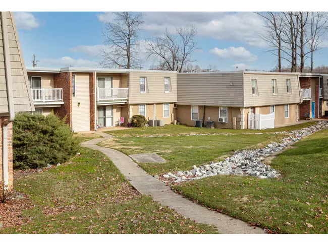 Apartment complex courtyard with grassy lawn, concrete paths, and beige buildings under a clear sky