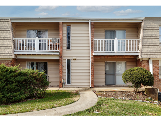 Two-story apartment building with balconies, front doors, and a curved walkway in front