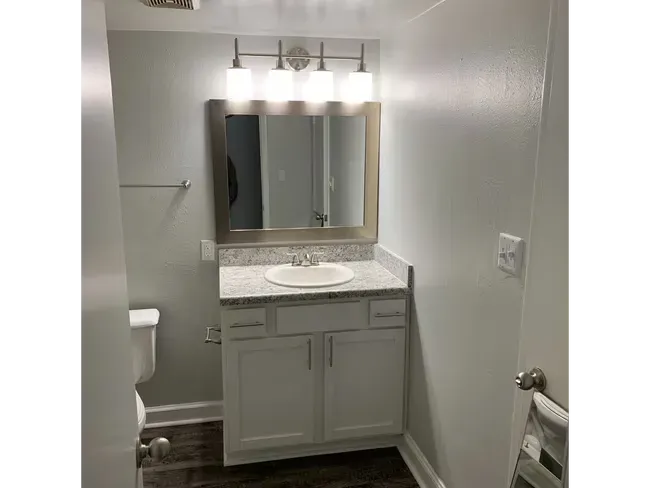 Small bathroom with white vanity, mirror, lights, toilet, and towel rack.