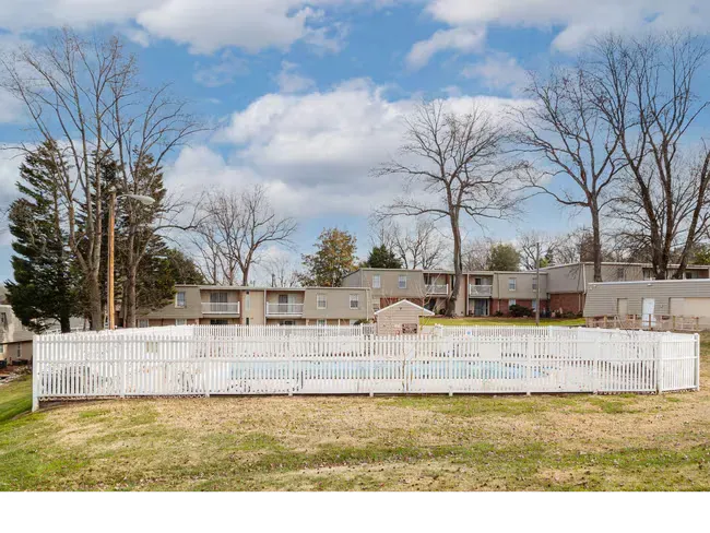 White-fenced backyard with a small above-ground pool in front of a row of houses and leafless trees