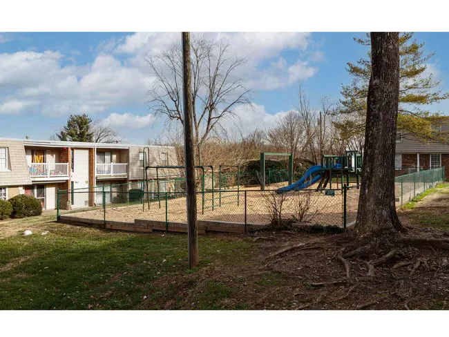Apartment courtyard with trees, grassy area, and a fenced playground with blue slide.