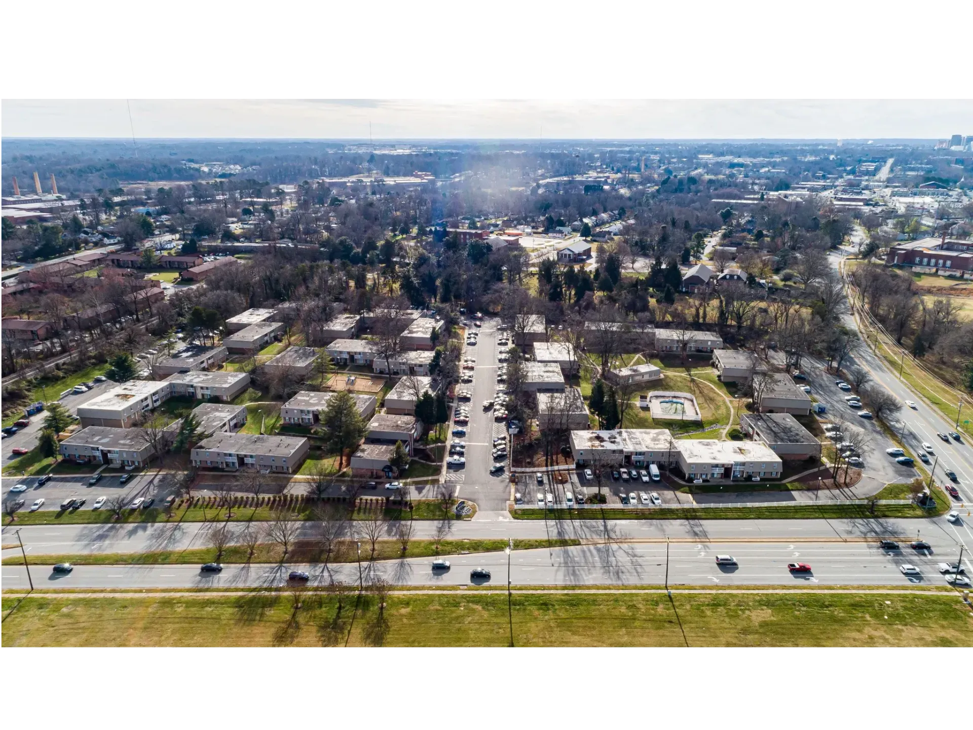 Aerial view of a suburban neighborhood with tree-lined streets, houses, and a busy road in the foreground