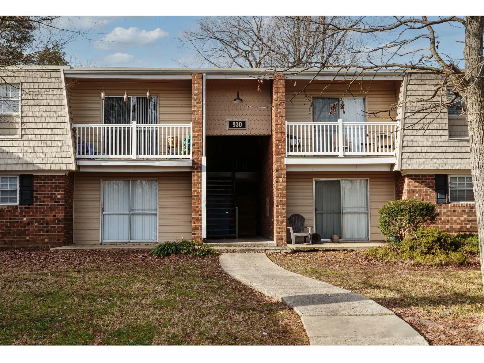 Apartment building entrance with brick facade, white balconies, and a curved sidewalk leading to the center doorway