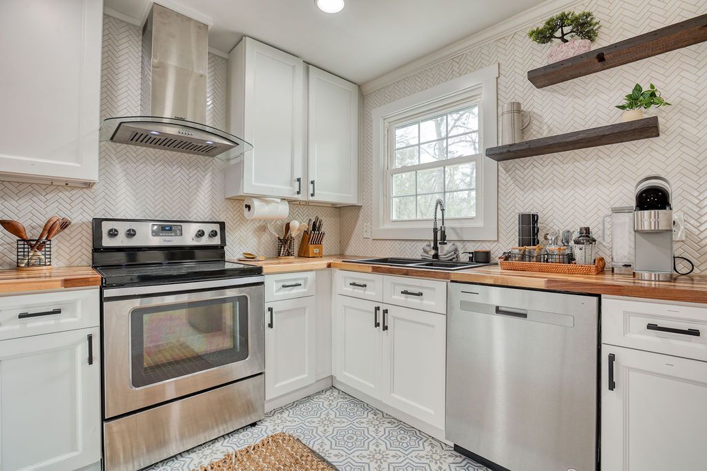 White kitchen with stainless steel appliances, butcher block counters, and patterned tile floor.