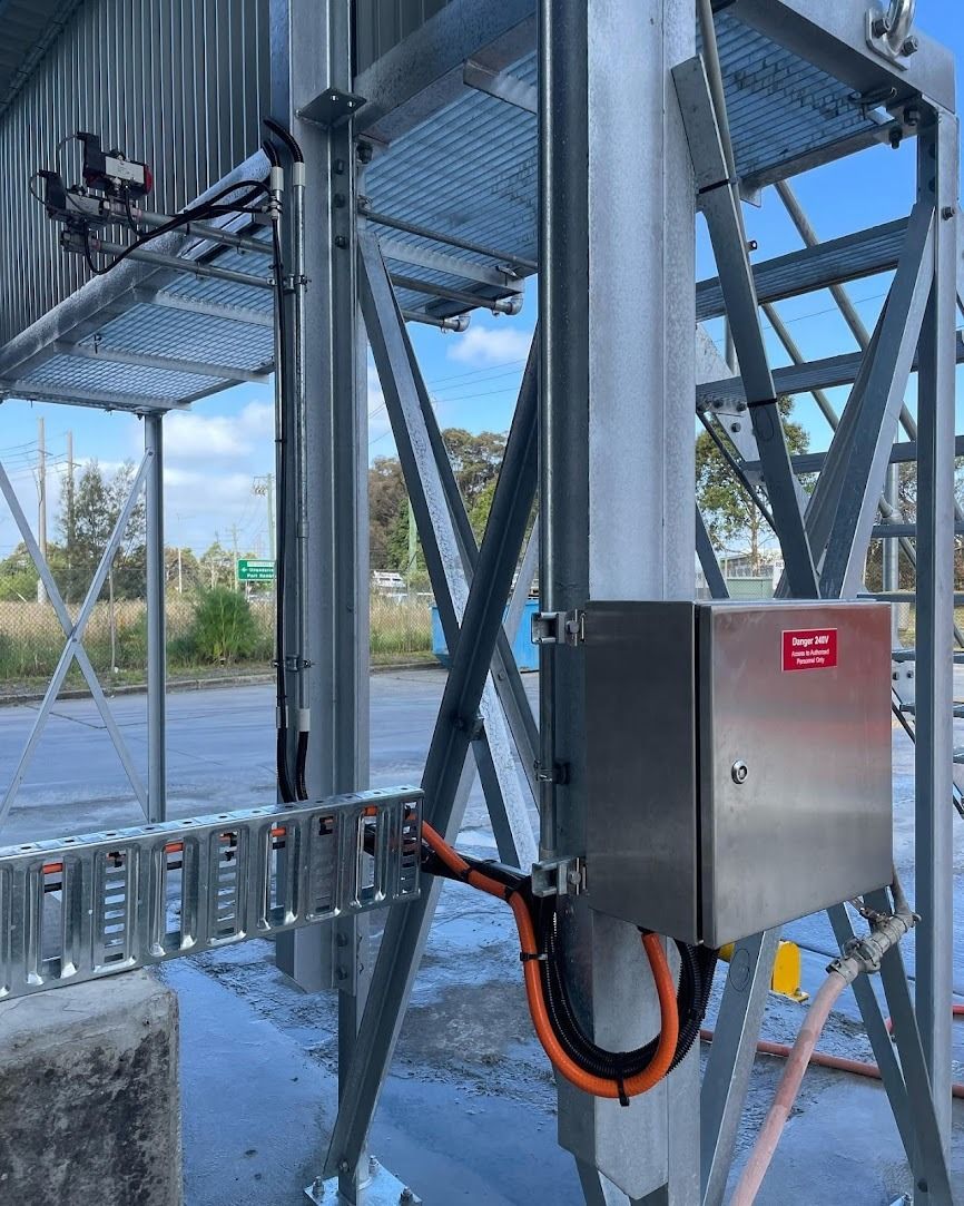 A stainless steel industrial control box mounted on a metal structural frame with orange cabling and metal cable trays.
