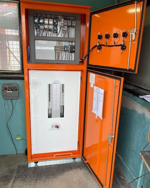 An industrial orange electrical cabinet with a white interior breaker panel and open door, mounted against a blue wall.