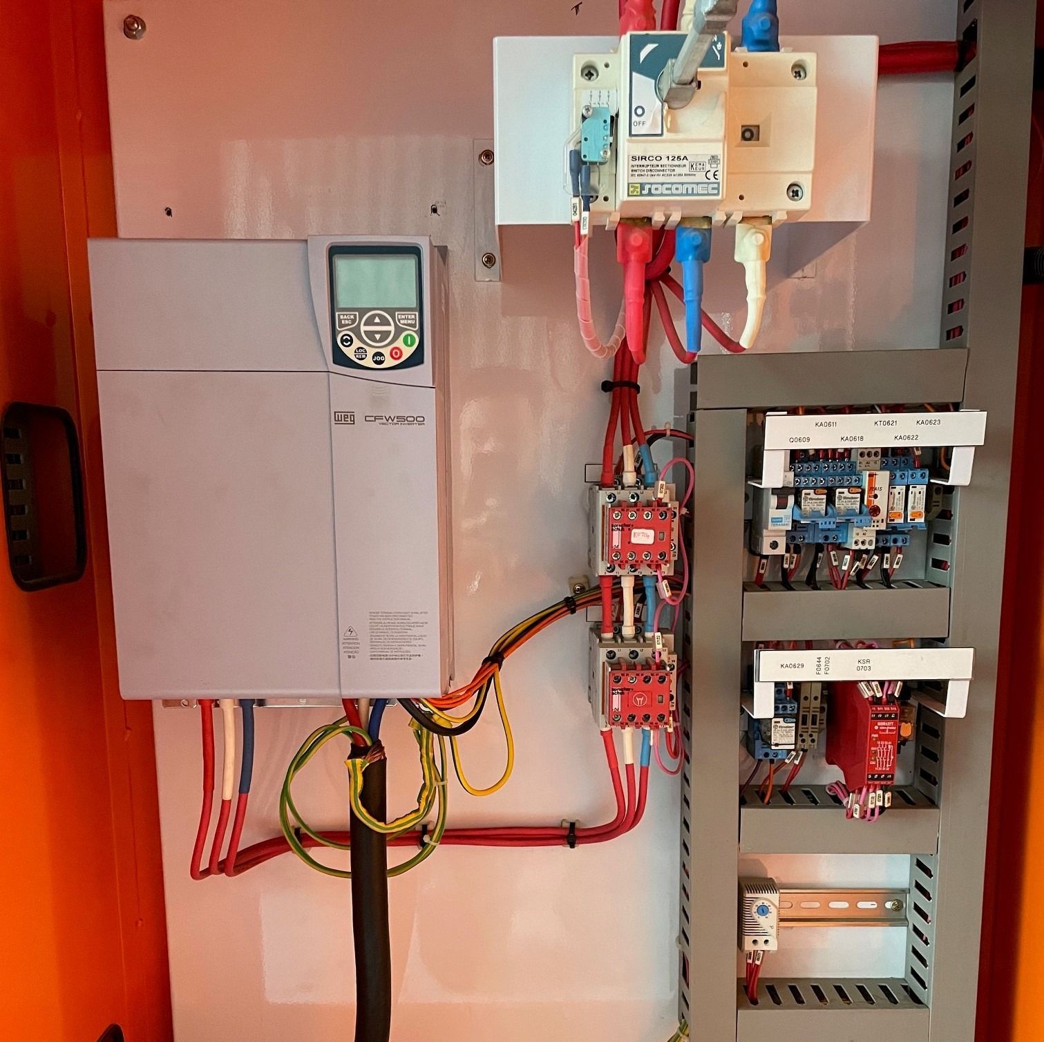 Electrical control panel featuring a variable frequency drive, a main disconnect switch, relays, and DIN rail terminals.