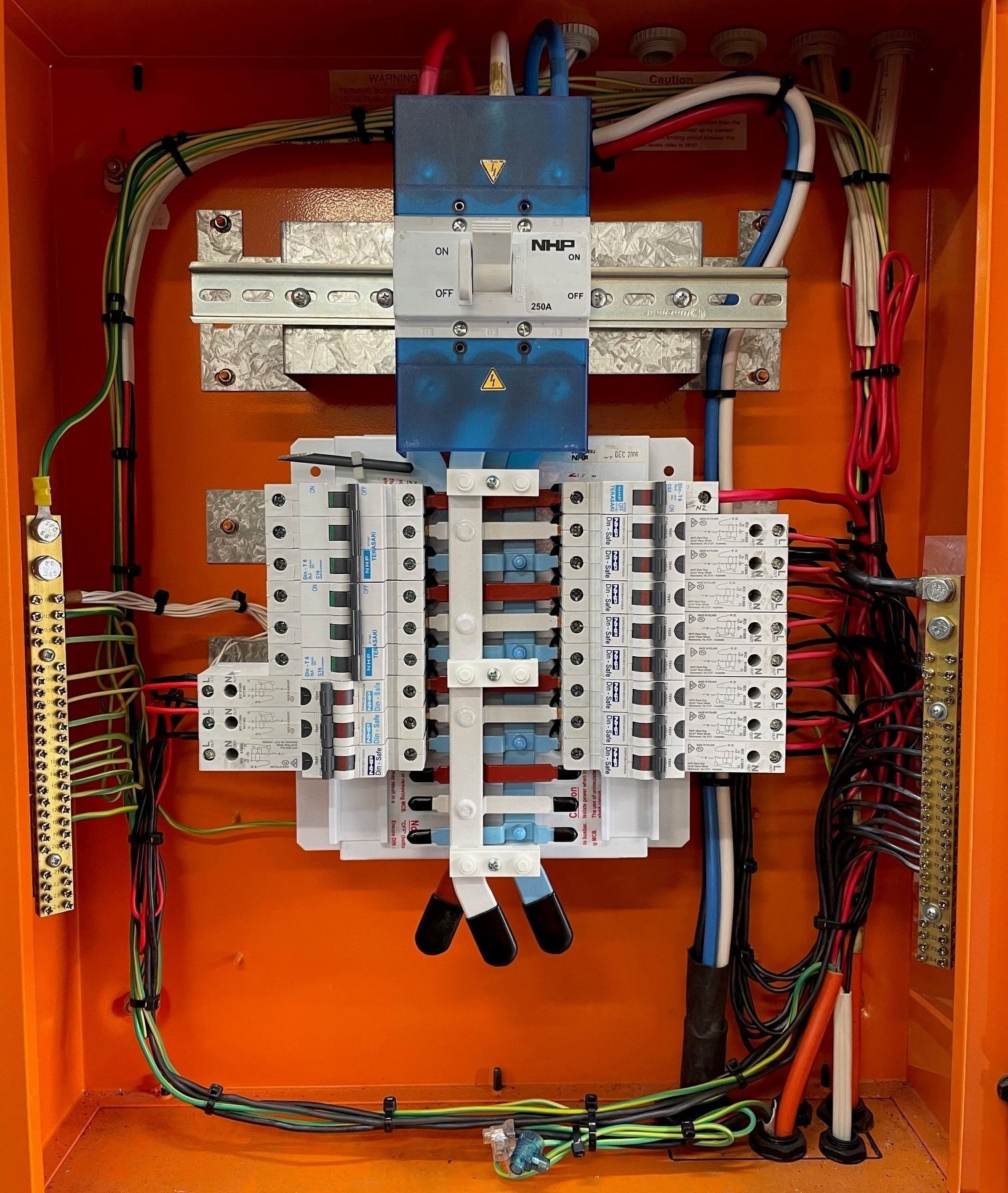 Inside view of an orange electrical distribution board featuring a main circuit breaker above a row of modular breakers.