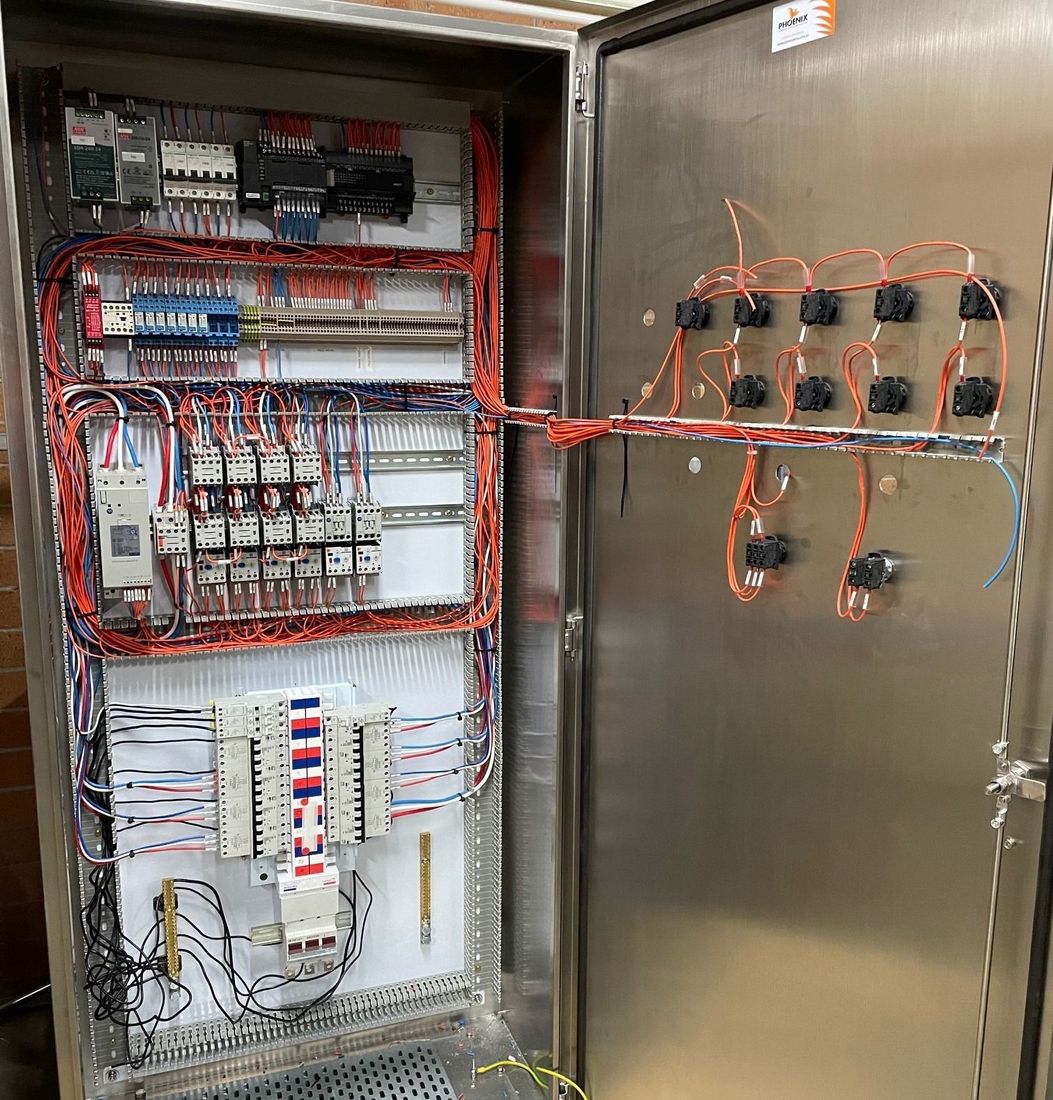 An open electrical control panel featuring neatly organized wiring, circuit breakers, relays, and door-mounted components.