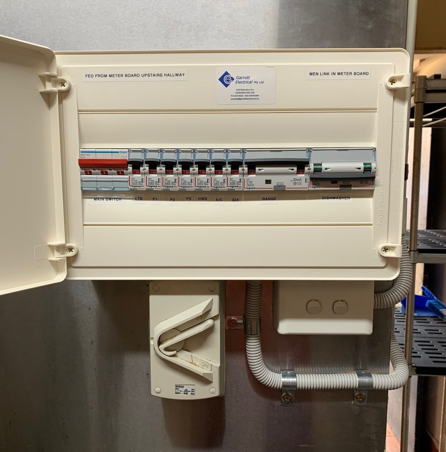 An open electrical distribution board with multiple circuit breakers mounted on a wall in a commercial setting.