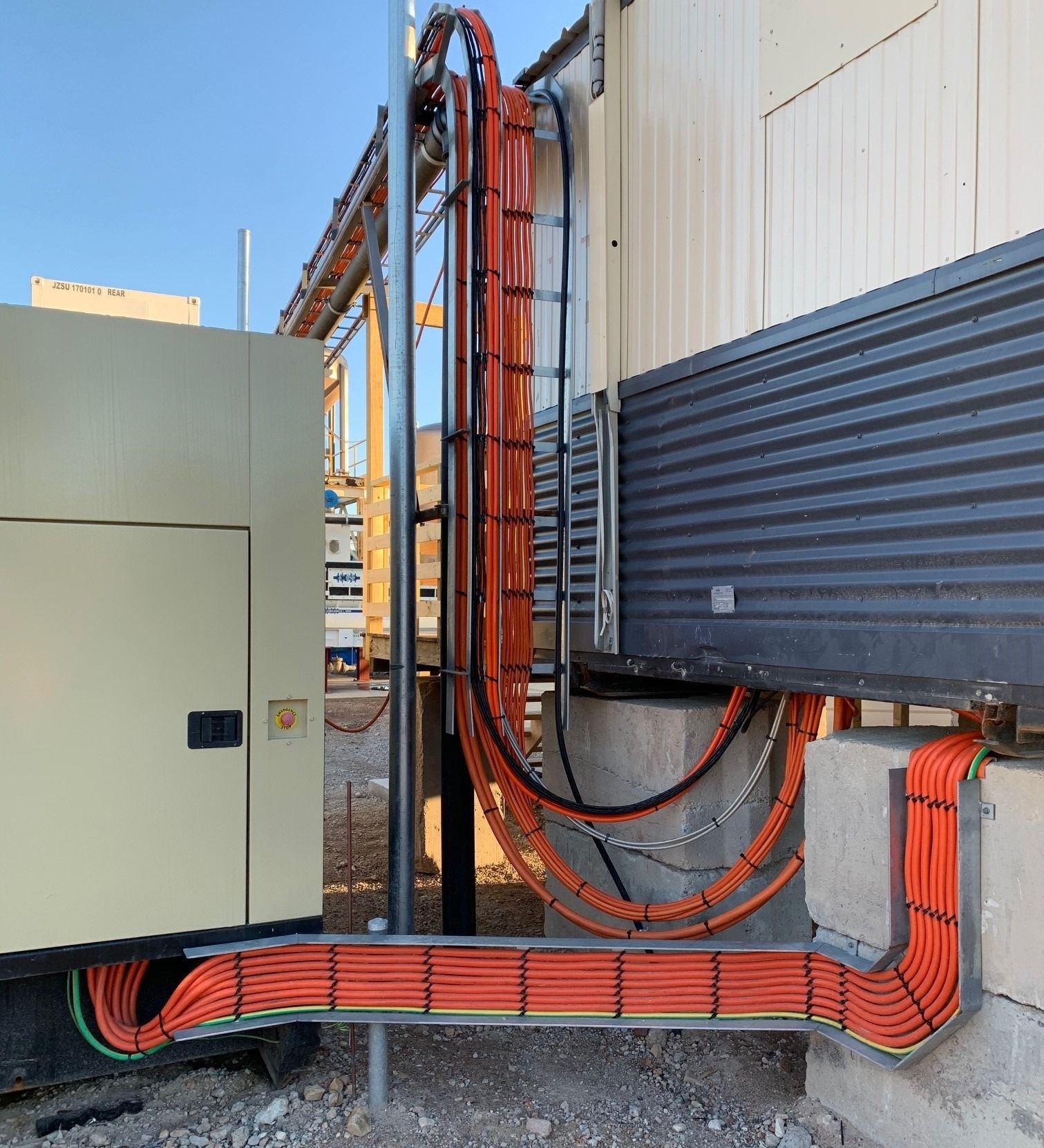 Orange electrical cables organized in metal trays running between a large cabinet and a building exterior.