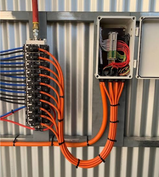 A technician wearing a hard hat and high-visibility vest checks electrical equipment using a handheld device and tablet.