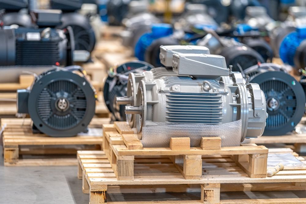 Rows of gray industrial electric motors stored on wooden pallets in a warehouse.